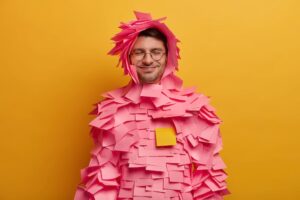 gars-positif-notes-adhesives-roses-collees-autour-du-corps-tete-fabrique-costume-papier-creatif-partir-autocollants-porte-lunettes-travaille-au-bureau-isole-mur-jaune-garde-yeux-fermes